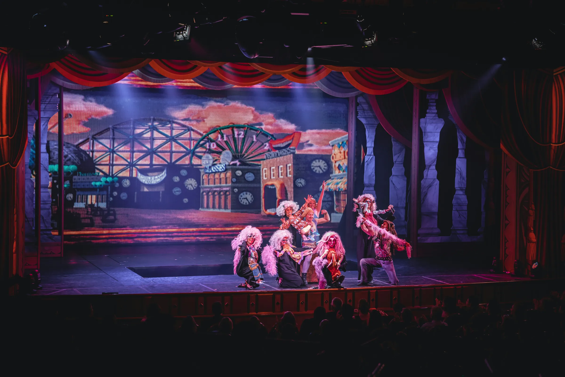 Cabaret performers in bright feathered and sequinned costumes under theatre spotlights